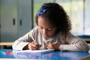 Menina parda focada sentada na mesa da escola e desenhando