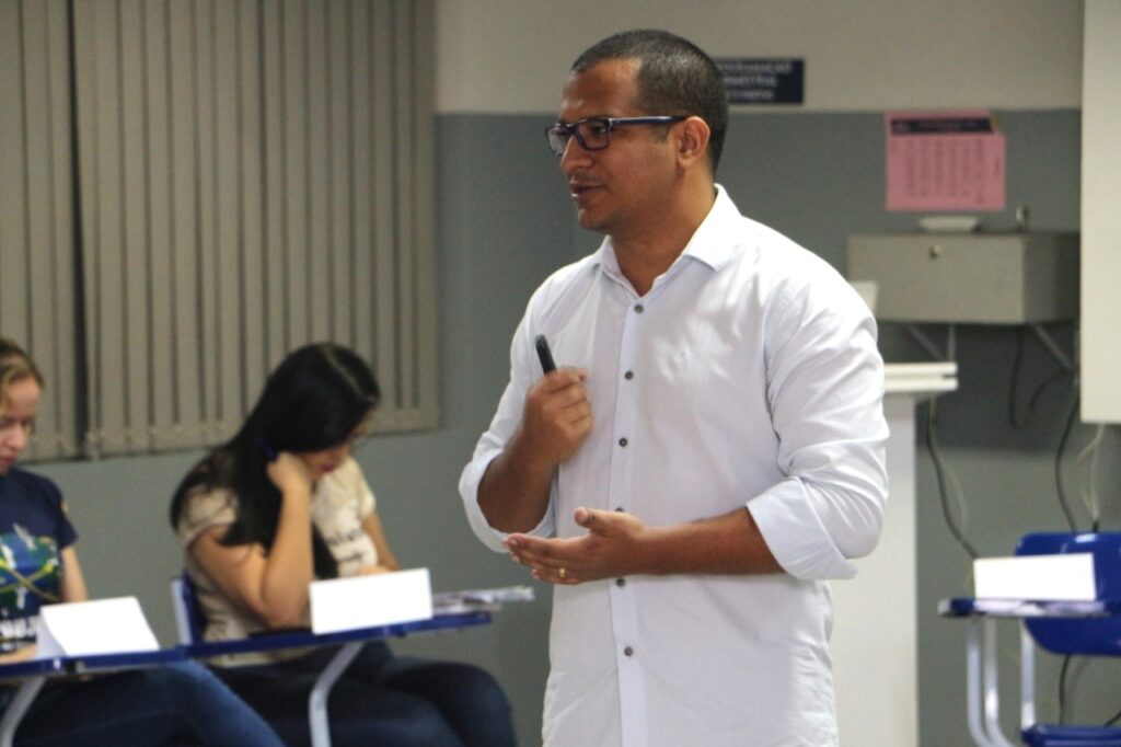 Professor Thomaz Edson Veloso vestido com camisa social branca, caminha pela sala enquanto palestra